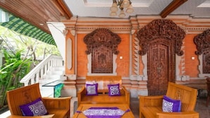 A traditional wooden bench and table set with patterned cushions, surrounded by intricately carved wooden doors and a staircase. - Ceria Guesthouse Seminyak Mitra RedDoorz (Bali)