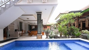 A swimming pool with a stone border, a reception area with a counter and chairs, and a staircase leading to an upper level. - Ceria Guesthouse Seminyak Mitra RedDoorz (Bali)