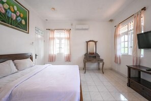 A bedroom with a bed, a dresser, a television, and a window with curtains. - Ceria Guesthouse Seminyak Mitra RedDoorz (Bali)