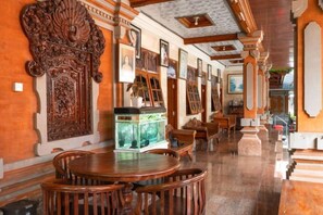 A room with a wooden dining table, chairs, a fish tank, and ornate wall decorations. - Ceria Guesthouse Seminyak Mitra RedDoorz (Bali)
