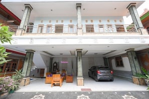 Un bâtiment à deux étages doté d’un porche, de colonnes et d’une voiture garée devant.