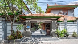 A traditional gate with a tiled roof, leading to a building with a tiled roof and a green awning. - Ceria Guesthouse Seminyak Mitra RedDoorz (Bali)