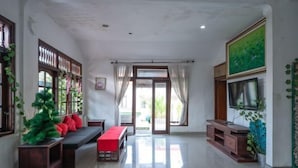 A spacious living room with a sofa set, a TV, and a large window with curtains. - Ceria Guesthouse Seminyak Mitra RedDoorz (Bali)