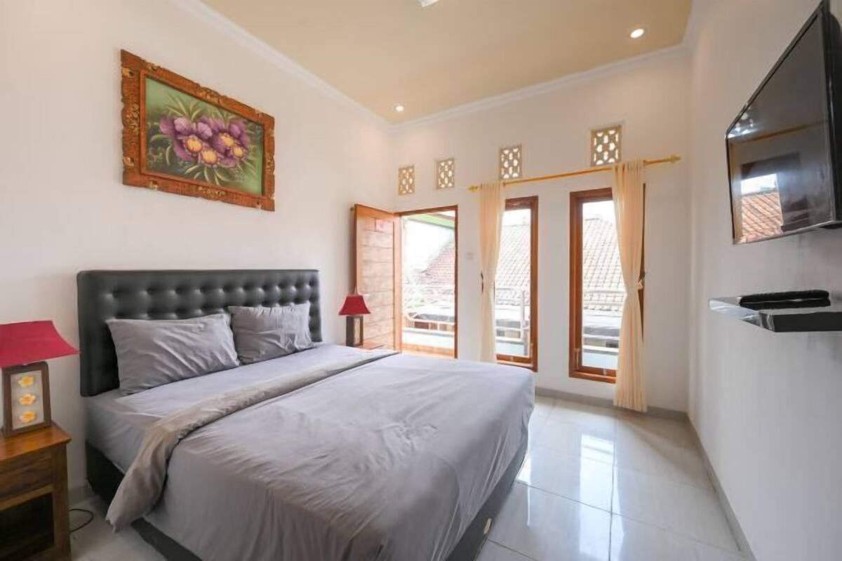 A bedroom with a large bed, a TV, a painting, and a view of the outside.