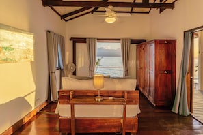A room with a bed, a wooden desk, a ceiling fan, a window with a view of the sea, and a wooden wardrobe. - Feel right at home in paradise in the eco friendly, off-grid home on Isla Colon. (Isla Colon)