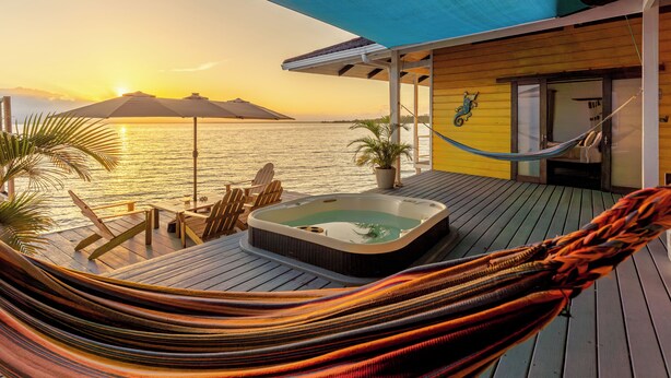 A hammock on a wooden deck with a hot tub and chairs, overlooking a body of water at sunset. - Feel right at home in paradise in the eco friendly, off-grid home on Isla Colon. (Isla Colon)