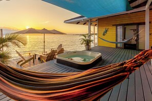 A hammock on a wooden deck with a hot tub and chairs, overlooking a body of water at sunset. - Feel right at home in paradise in the eco friendly, off-grid home on Isla Colon. (Isla Colon)