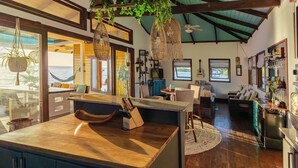 A spacious living area with a large wooden island, a hammock by the window, and a view of the ocean. - Feel right at home in paradise in the eco friendly, off-grid home on Isla Colon. (Isla Colon)