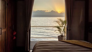 A room with a bed, a potted plant, and a view of the sea at sunset. - Feel right at home in paradise in the eco friendly, off-grid home on Isla Colon. (Isla Colon)