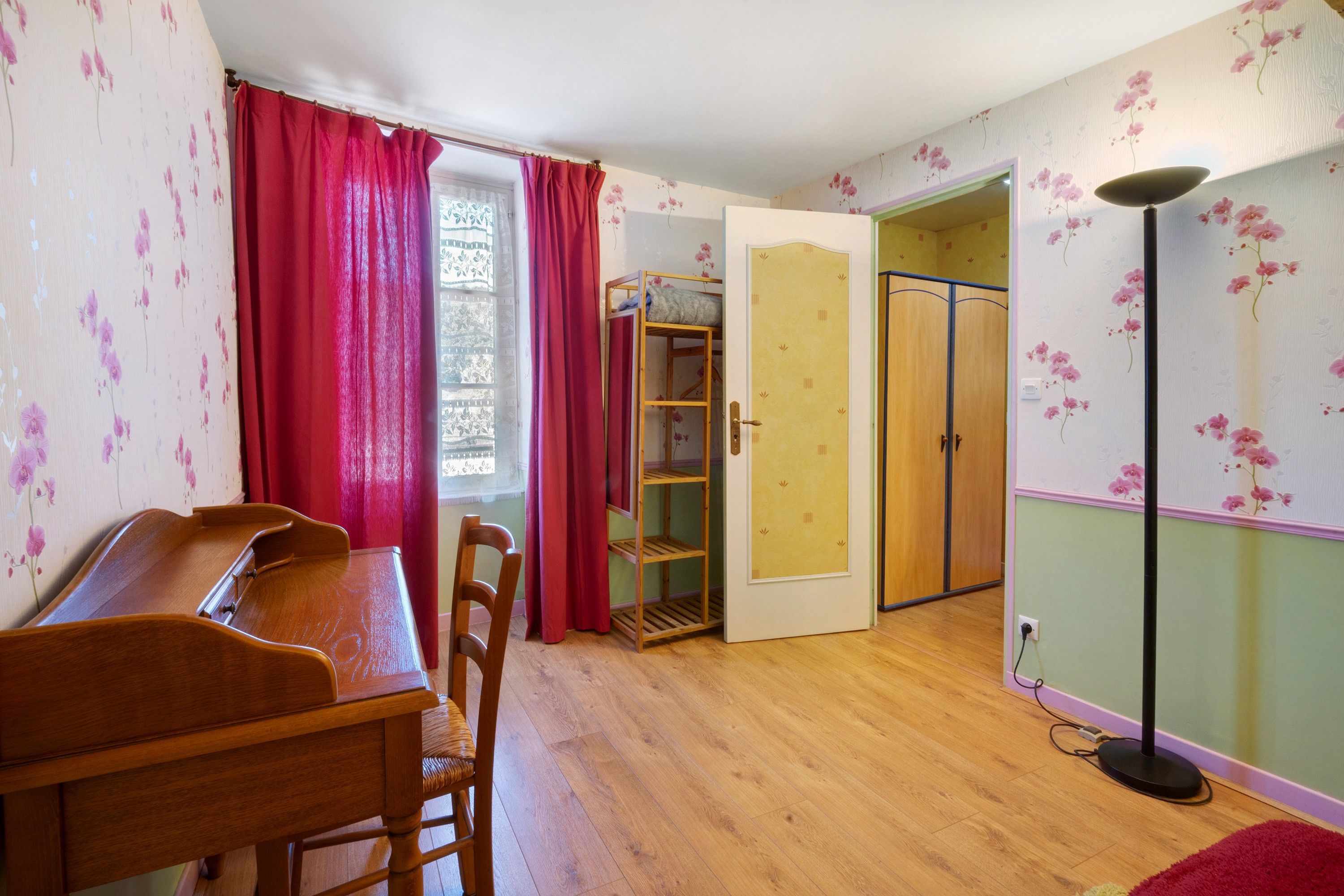 A room with a wooden desk, chairs, a wardrobe, and a floor lamp.
