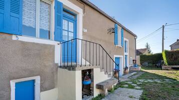 A two-story building with blue shutters, a stone staircase, and a small garden area with a bench.