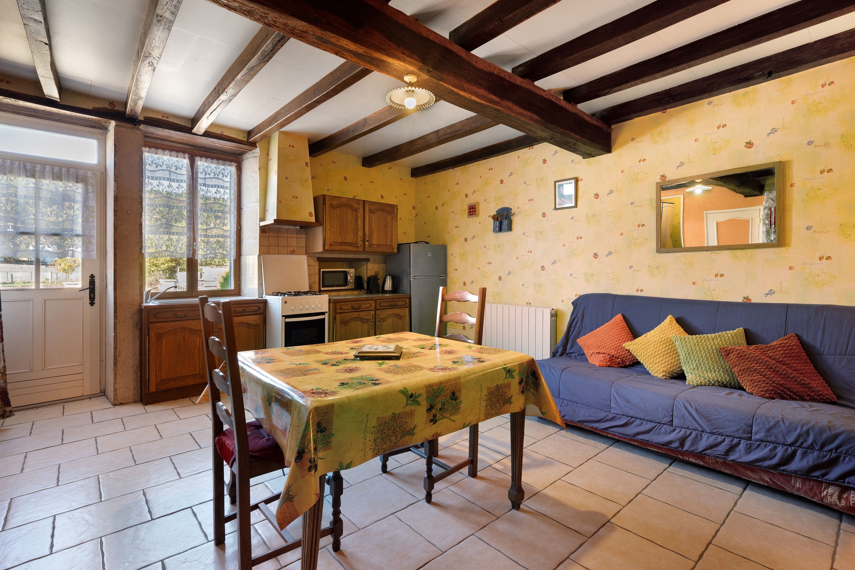 A cozy kitchen with wooden cabinets, a dining table with a floral tablecloth, and a blue sofa with colorful cushions.