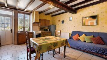 A cozy kitchen with wooden cabinets, a dining table with a floral tablecloth, and a blue sofa with colorful cushions.
