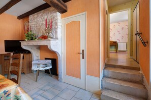 A room with a stone wall, a wooden door, a television, a table with a lace tablecloth, and a staircase leading to another room. - Gîte “Chez Manon” with Private Garden (Massangis)