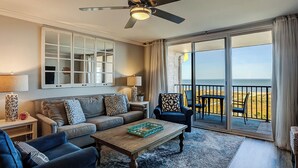 A living room with a sofa, armchairs, a coffee table, a ceiling fan, a large window with a view of the beach, and a sliding glass door. - Sunset Rentals | Island Club 2403 (Hilton Head Island)