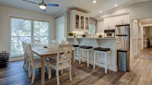 Une cuisine moderne avec des meubles blancs, un réfrigérateur en acier inoxydable et un coin repas comprenant des chaises et une table en bois.