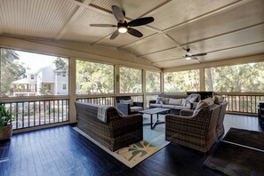 A covered patio with wicker furniture, ceiling fans, and large windows offering views of a residential area. - Sunset Rentals | Elderberry 3 (Hilton Head Island)