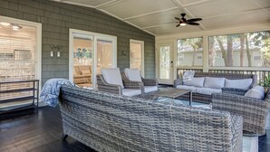Une terrasse couverte, aménagée avec des meubles en osier, des ventilateurs de plafond et offrant une vue sur l’extérieur.