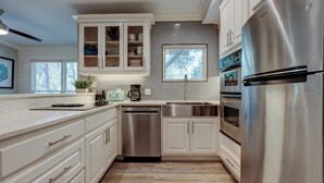 Une cuisine moderne avec des meubles blancs, des appareils en acier inoxydable et une fenêtre donnant sur un espace verdoyant.