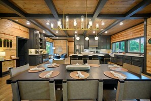 Una cocina moderna con armarios oscuros, una isla central y un comedor con mesas y sillas redondas.