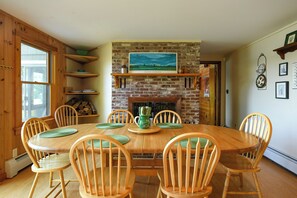 A dining room with a brick fireplace, wooden chairs, and a table set for six. - Spacious 7-Bedroom Lakeside Retreat on Little Sebago Lake (Raymond)