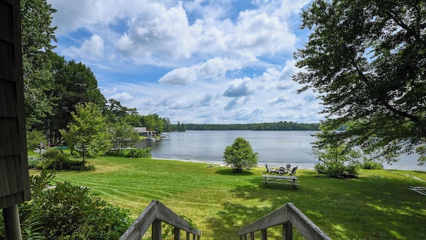 Blick vom Balkon auf einen See mit Holzterrasse, Picknicktisch und Bootssteg.