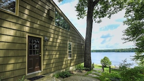Ein Haus mit brauner Tür und Fenstern, einem Steinweg und Blick auf einen See.