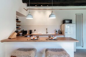 Une cuisine moderne avec un plan de travail en bois, deux suspensions lumineuses, un four à micro-ondes, un réfrigérateur et un évier.