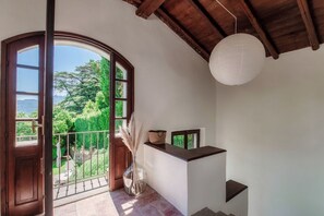 Une pièce avec une porte en bois donnant sur un balcon, un vase blanc contenant de la pampa et une lanterne en papier blanche suspendue au plafond.