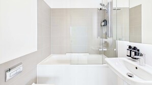 A modern bathroom with a glass-enclosed shower, a white bathtub, and a sink with a mirror. - Light-filled Camden Town Balcony Apartment (Greater London)