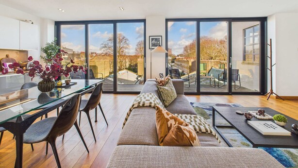 A spacious living area with a large glass door leading to an outdoor balcony, a dining area with a glass table, and a cozy seating arrangement with a sofa and cushions. - Light-filled Camden Town Balcony Apartment (Greater London)