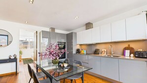 A modern kitchen with a glass dining table, grey cabinets, and a view to the outside. - Light-filled Camden Town Balcony Apartment (Greater London)
