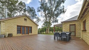 Un espacio al aire libre techado con una terraza de madera, una mesa con sillas y un edificio de piedra con chimenea.