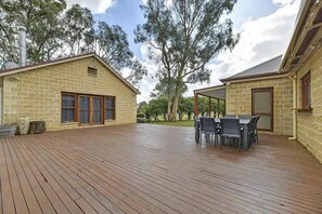 A covered outdoor area with a wooden deck, a table with chairs, and a stone building with a chimney. - Fallenwood (Orange)