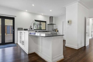 A modern kitchen with white cabinetry, a central island, and a large window. - Fallenwood (Orange)