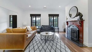 Una sala de estar con sofá, sillón, mesa de centro, chimenea y ventanas amplias.