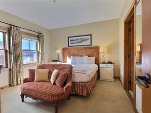 A hotel room with a bed, a chair, a nightstand, a lamp, and a door. - Mountaineer Square 313 | 1BR Walk-to-Lifts Condo, Sleeps 4, Pool & Hot Tub (Crested Butte)