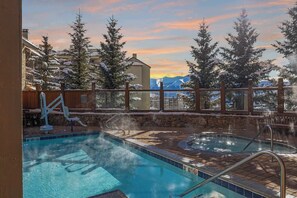 Ein Poolbereich mit Whirlpools, einer Holzterrasse und Blick auf schneebedeckte Bäume und Berge.