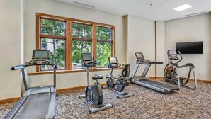 A fitness room with treadmills, stationary bikes, and a TV screen. - Mountaineer Square 313 | 1BR Walk-to-Lifts Condo, Sleeps 4, Pool & Hot Tub (Crested Butte)