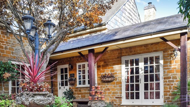 A stone building with a covered porch, potted plants, and a sign reading 'Russell Cottage.' - 1 bedroom accommodation in Flore (Flore)