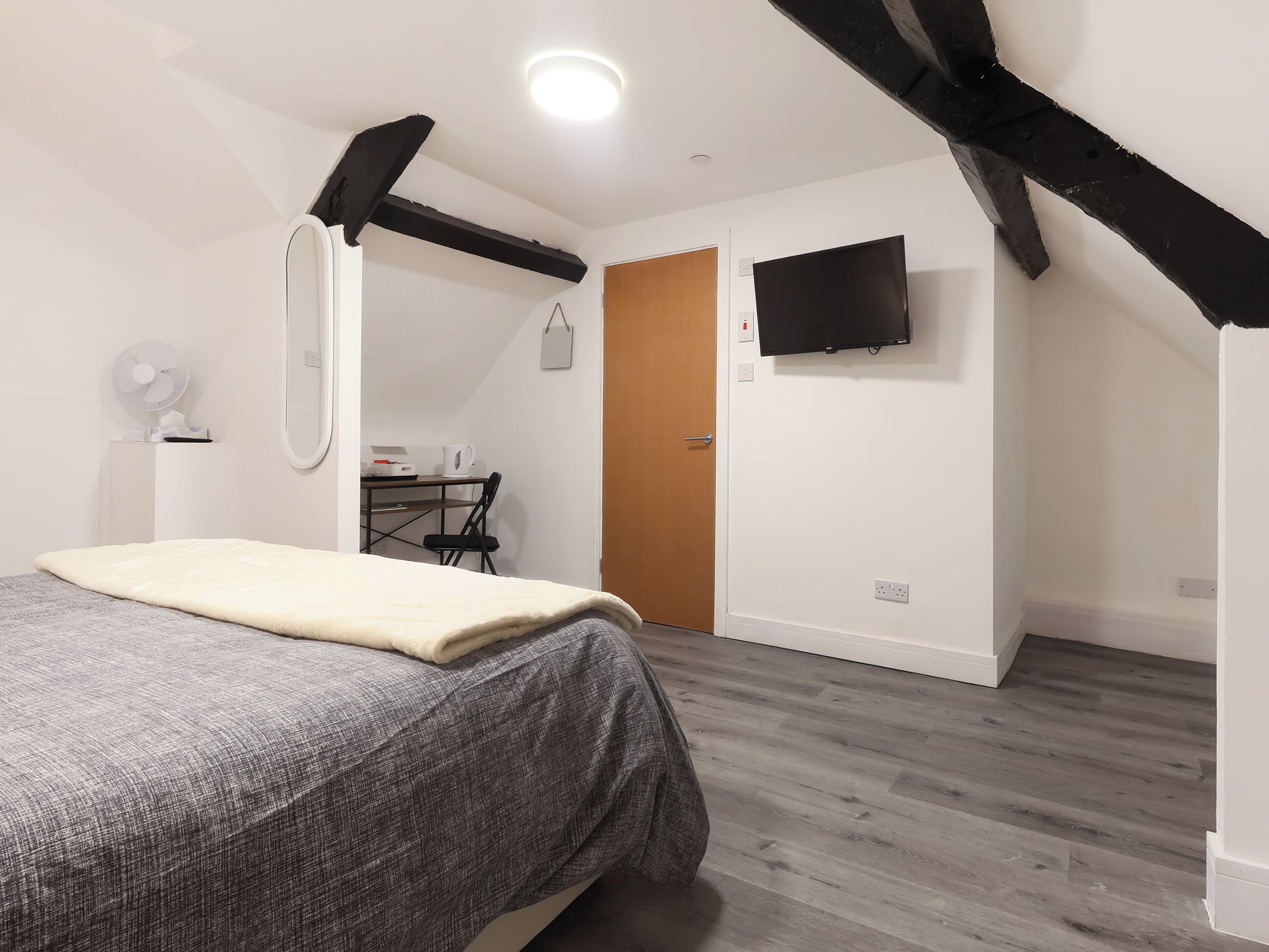Ein Schlafzimmer mit Bett, Schreibtisch, Stuhl, Fernseher und Holzboden.