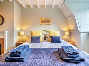 Une chambre à coucher comprenant un lit, deux tables de chevet, des lampes, un tableau encadré au mur et une fenêtre sous un plafond en pente.
