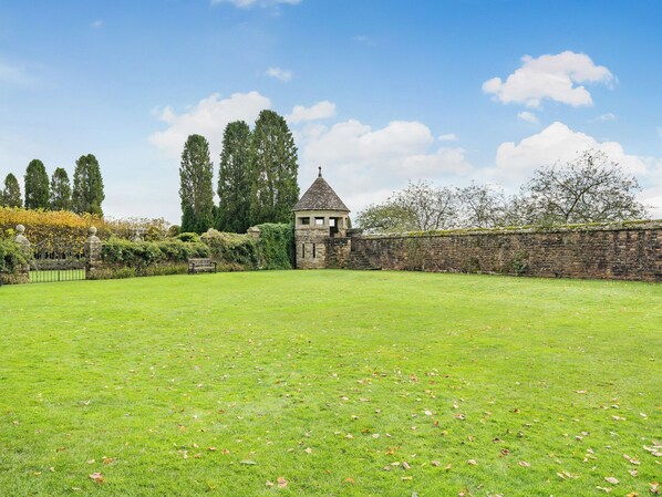 A grassy courtyard with a stone wall, a small tower-like structure, and a bench.