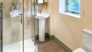 Casa de banho com cabine de duche em vidro, lavatório suspenso, espelho e janela com cortina estampada.