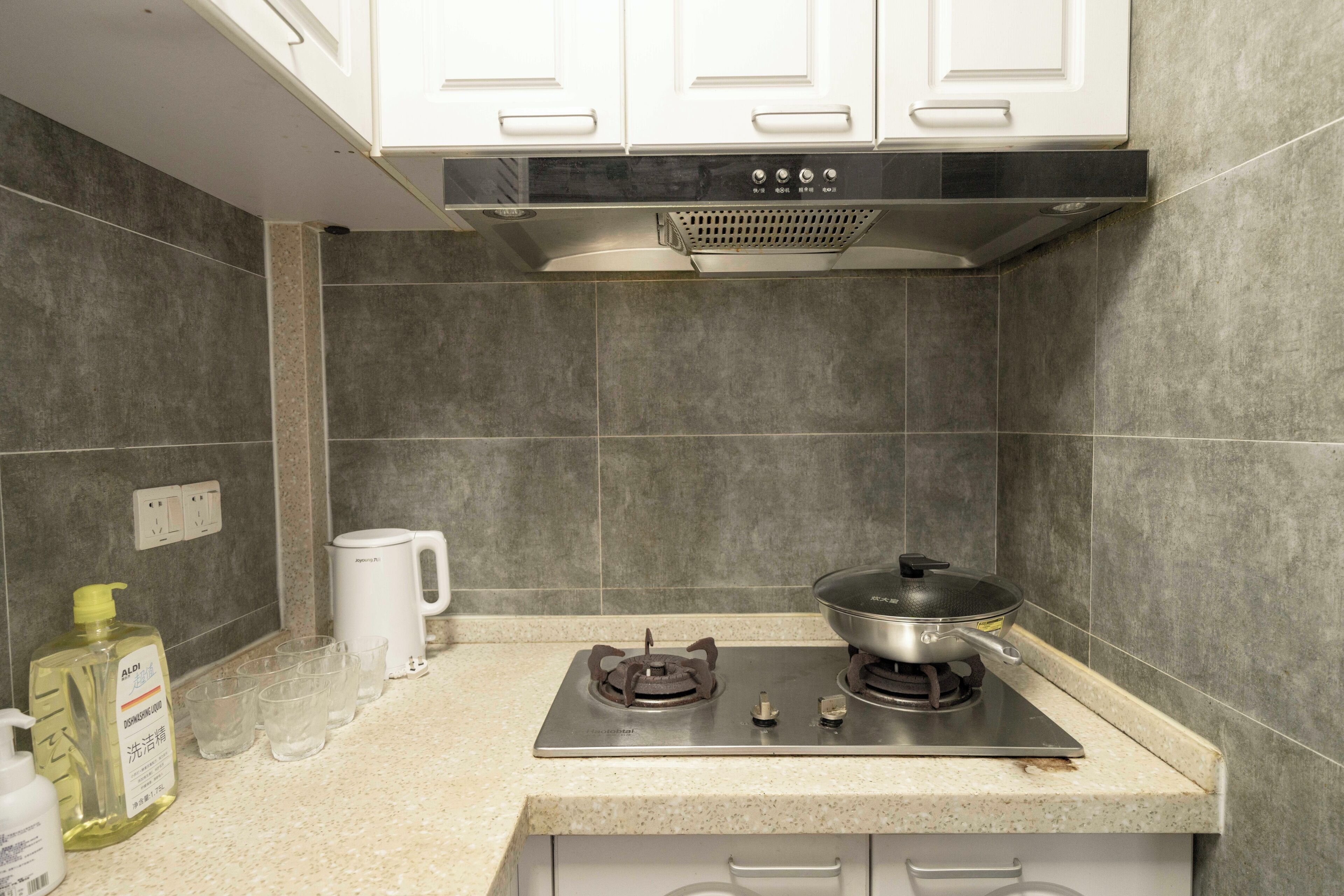 A kitchen with a gas stove, a kettle, and a bottle of dish soap.