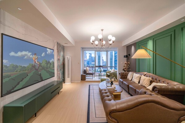 A modern living room with a large flat-screen TV, leather sofas, a chandelier, and a view of the city through large windows. - Book and Bed - North Bund (Shanghai)