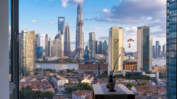 A cityscape view from a high-rise hotel room with a large window, a vase with flowers, and a wooden side table. - Book and Bed - North Bund (Shanghai)