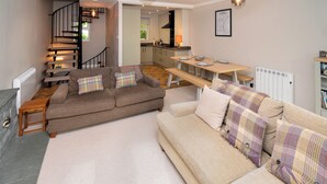 Amplia sala de estar con un conjunto de sofás, una mesa de comedor y una escalera que lleva a un piso superior.
