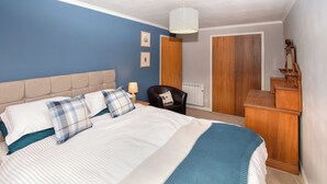 Un dormitorio con cama, una silla, cómoda y puerta.
