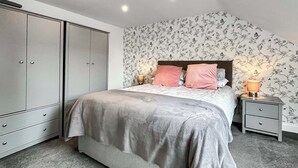 Een slaapkamer met een bed, nachtkastjes, een kledingkast en bloemenbehang.